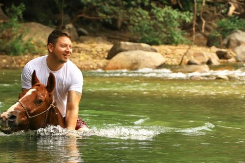 Diplo riding a horse in a river