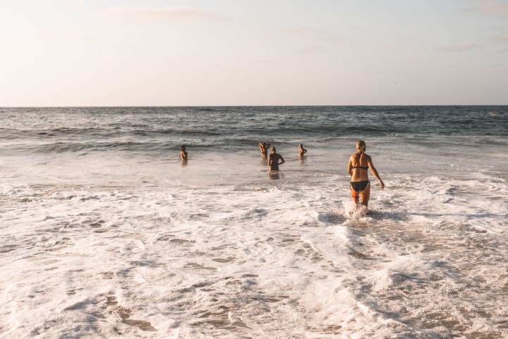 a man walking across a beach next to the ocean